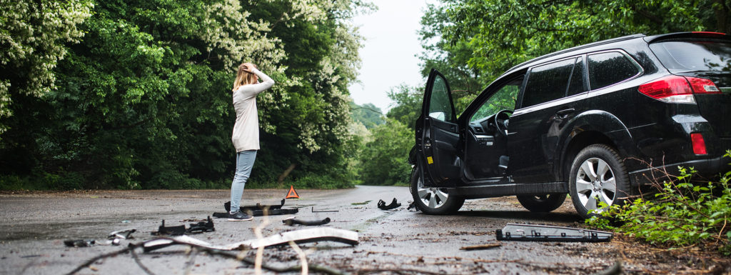 Young woman standing by the damaged car after a car accident.