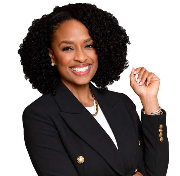 Woman with curly black hair smiles, wearing a black blazer with gold buttons and a white top. She stands against a light background with one arm bent and hand near her face, displaying confidence.
