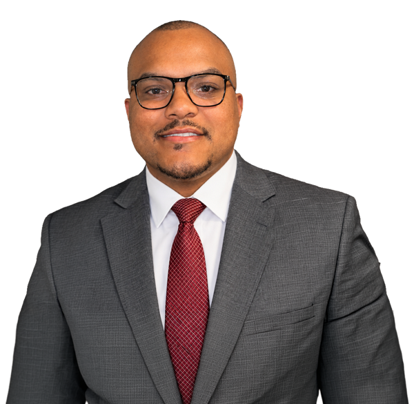 A man wearing glasses, a gray suit, a white shirt, and a red patterned tie stands against a plain white background, smiling at the camera.